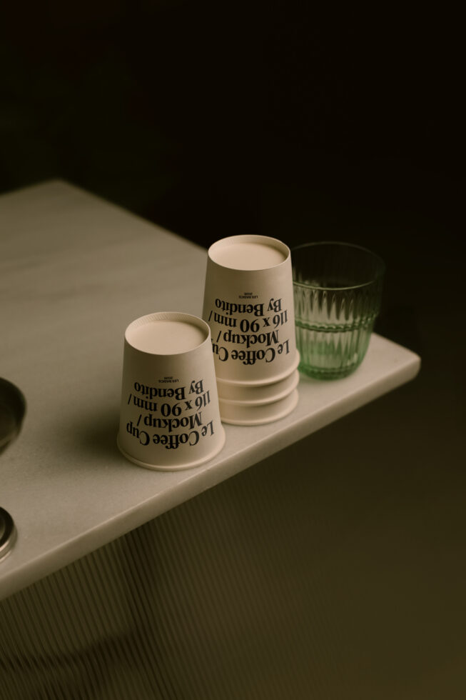 Sage green paper cups with typography print styled with green glass on white surface