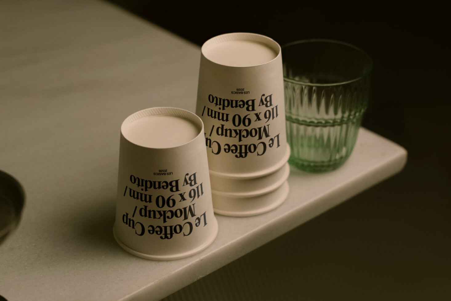 Minimalist setup of sage paper cups with text design alongside green glassware