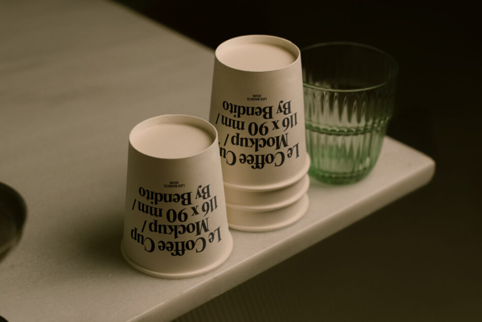 Minimalist setup of sage paper cups with text design alongside green glassware