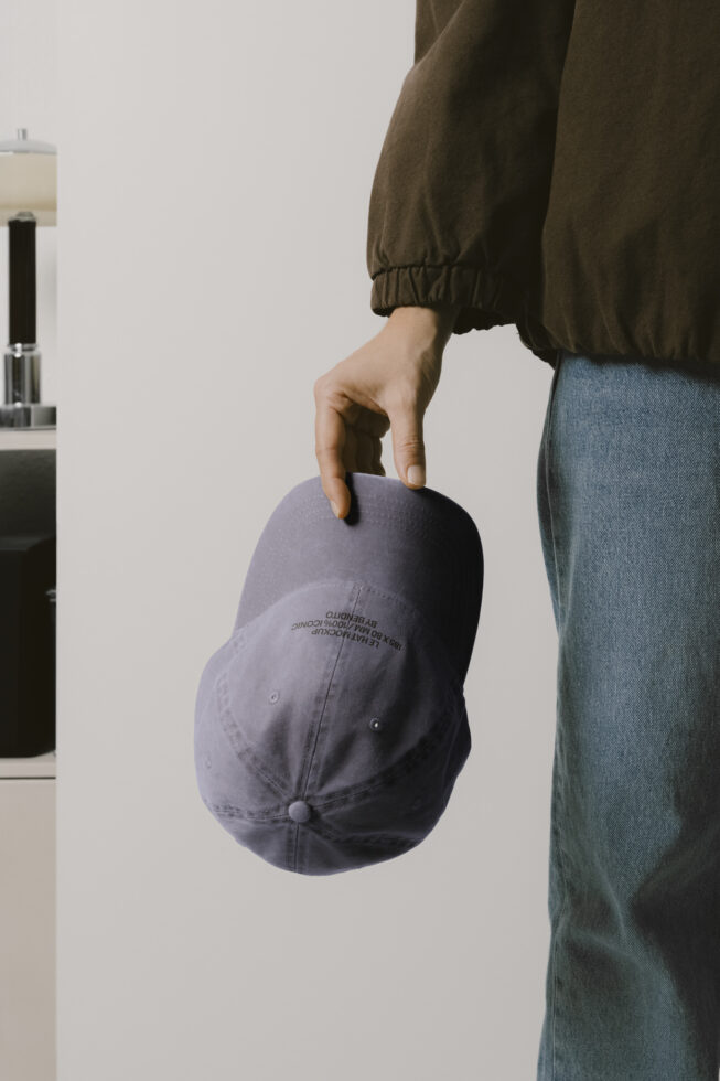 Hand holding lavender baseball cap with embroidered Bendito Les Basics text