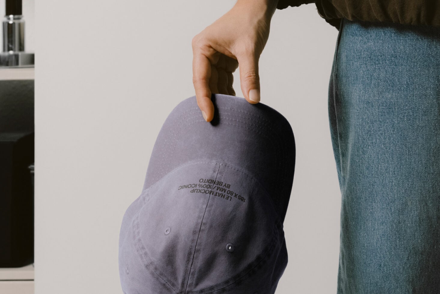 Slate baseball cap held in hand showing embroidered text on curved brim