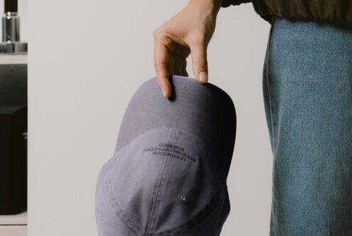Slate baseball cap held in hand showing embroidered text on curved brim