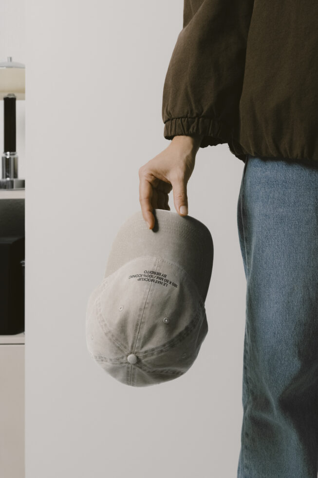 Person holding cream colored cap showing embroidered Bendito branding on back