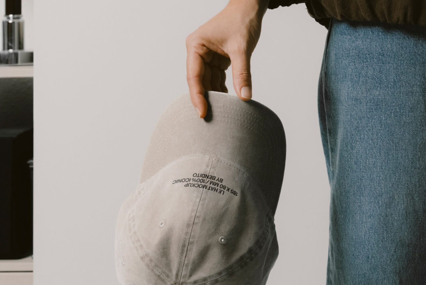 Cream colored baseball cap held in hand displaying embroidered text on brim