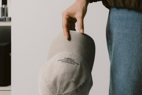 Cream colored baseball cap held in hand displaying embroidered text on brim