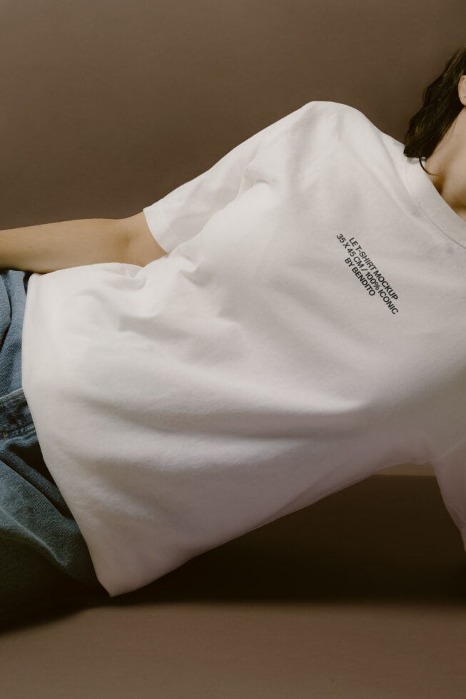 White oversized t-shirt with tiny text detail, modeled on brown background