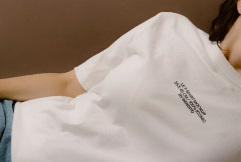 White relaxed fit shirt with small graphic on chest, worn on warm brown backdrop