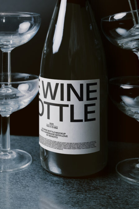 Dark wine bottle mockup with white label, surrounded by filled cocktail glasses
