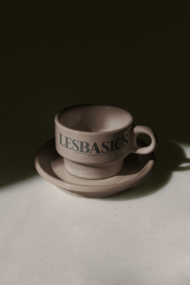 White ceramic coffee cup with saucer showing LE BASICS branding in serif type