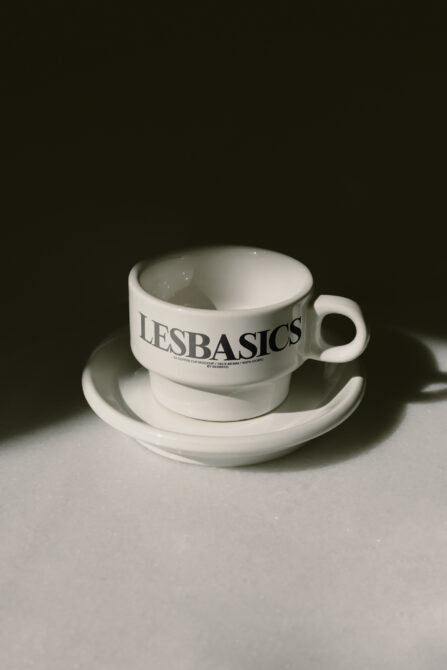 White porcelain tea cup on saucer with LE BASICS text displayed against dark backdrop