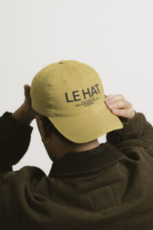 Olive green baseball cap with LE HAT branding text worn by person in olive jacket