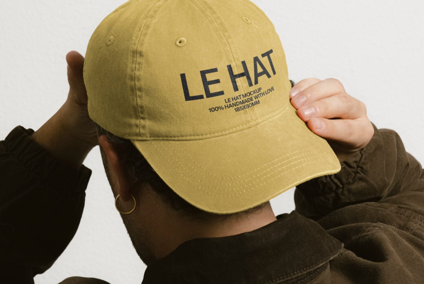 Mustard yellow baseball cap with LE HAT text held up by person's hands