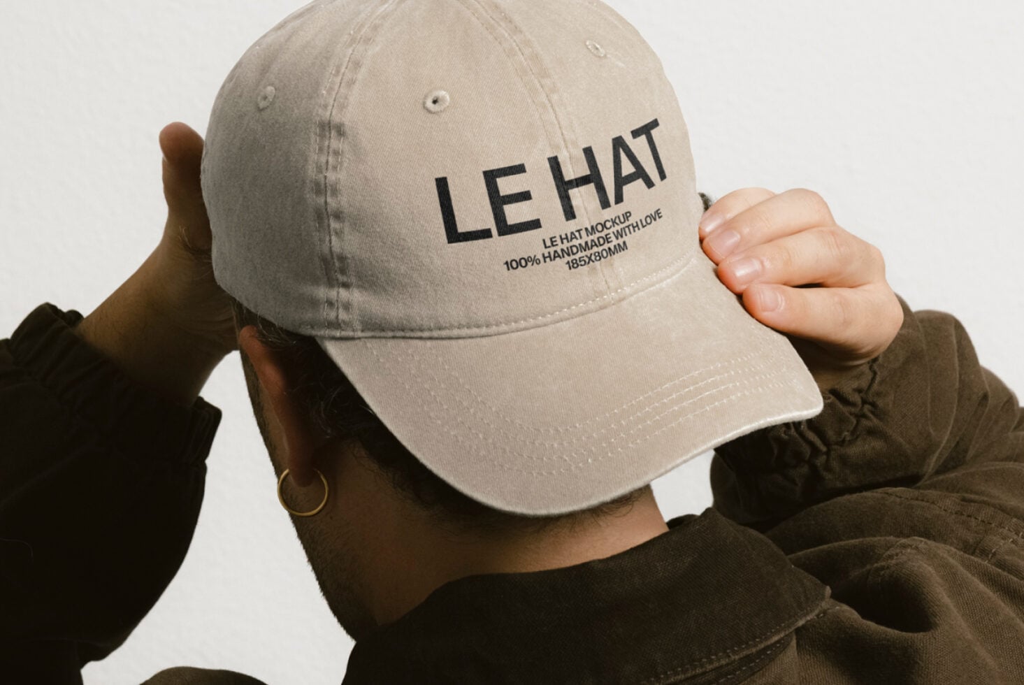 Cream colored baseball cap with LE HAT text held up by person's hands