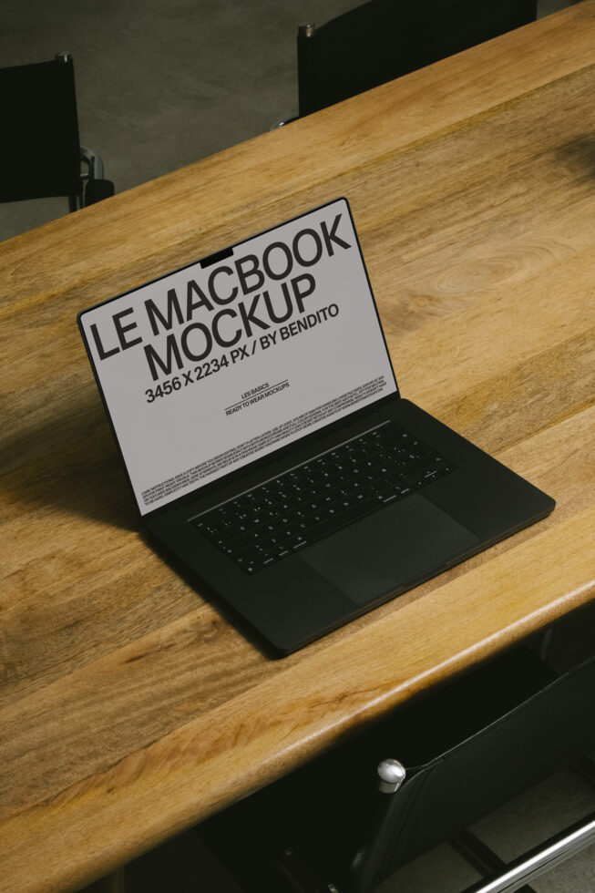 Light gray MacBook screen on wood table showing editable mockup layout design