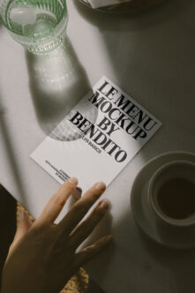 White leaflet mockup held by hand next to beverage, natural light