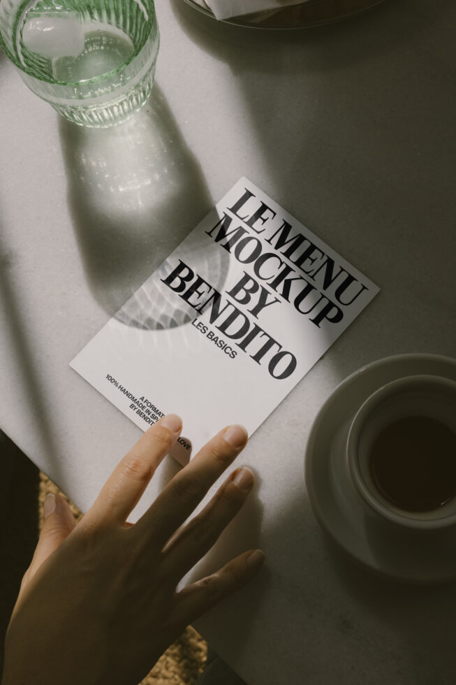 White leaflet mockup held by hand next to beverage, natural light