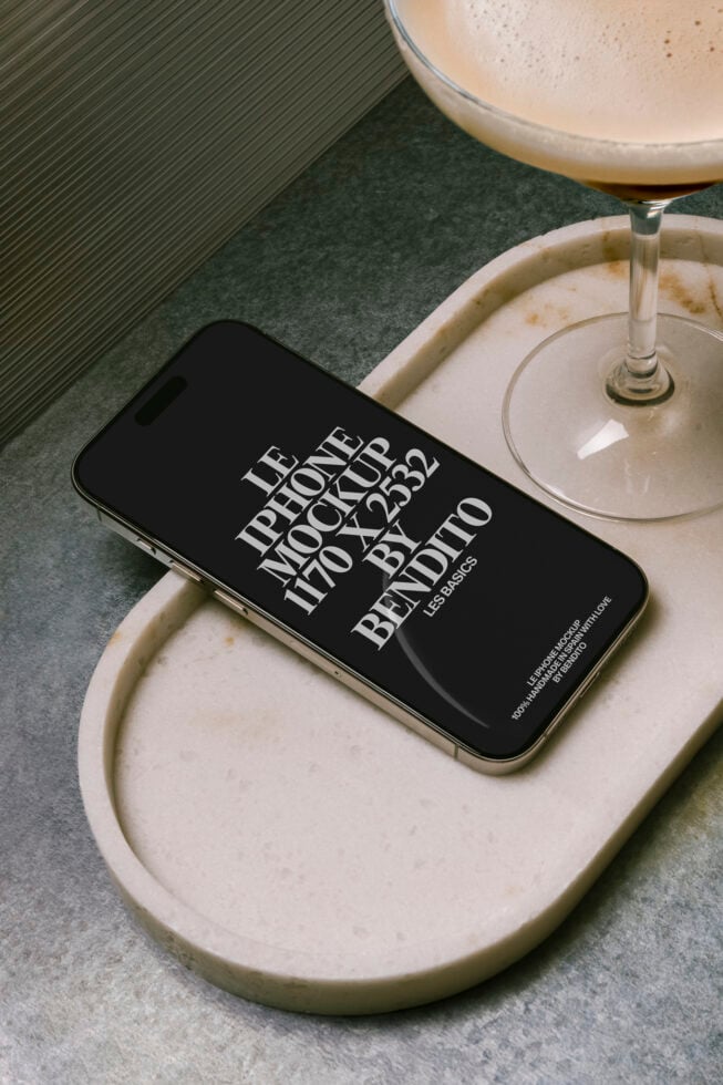 Black iPhone on cream ceramic dish next to cocktail glass with ribbed background
