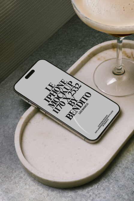 White iPhone on cream ceramic dish next to cocktail glass with ribbed background