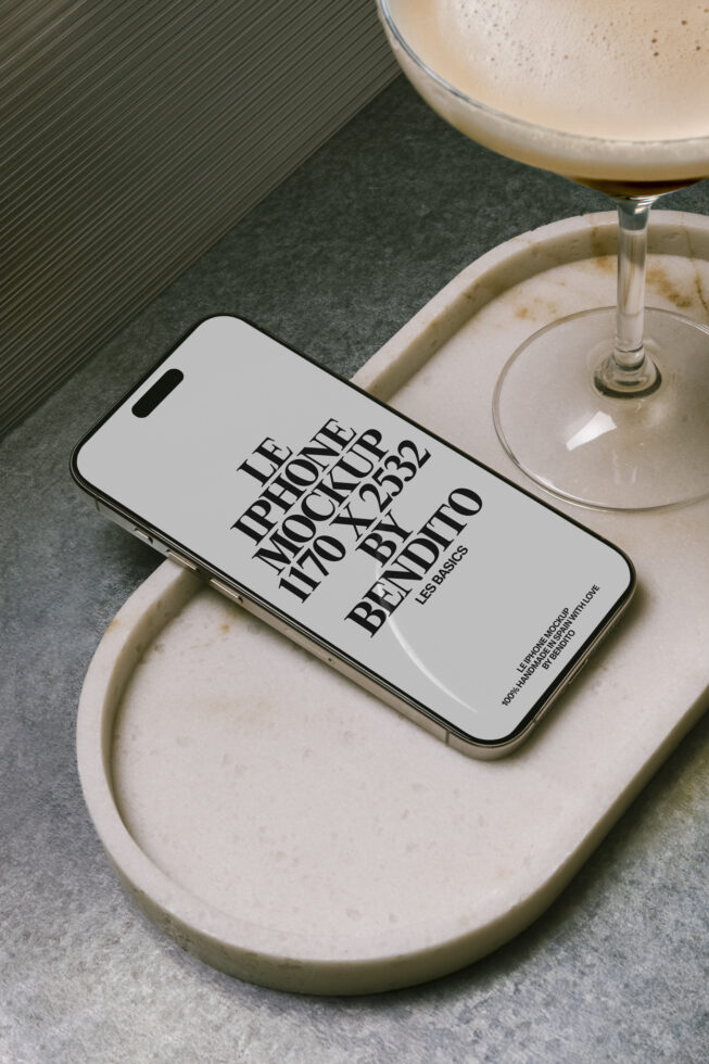 White iPhone on cream ceramic dish next to cocktail glass with ribbed background