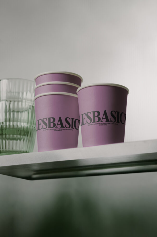 Purple coffee cups with Les Basics branding on white shelf with glass