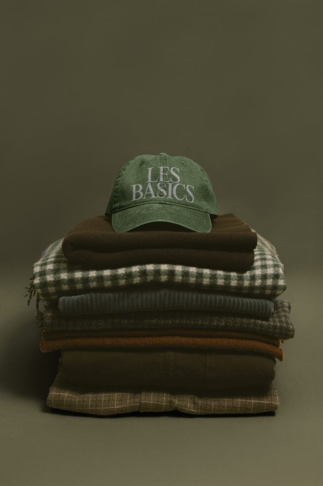 Washed green cap on stack of folded sweaters, knitwear in earthy neutral tones