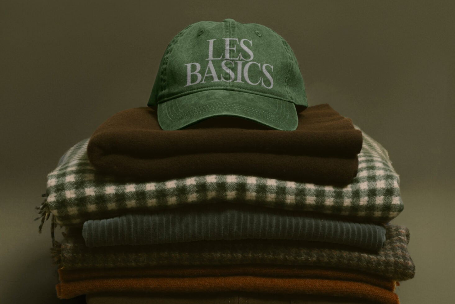 Green vintage cap with Les Basics text stacked on folded sweaters