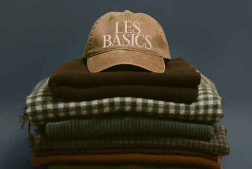 Tan vintage cap with Les Basics text on pile of knit sweaters