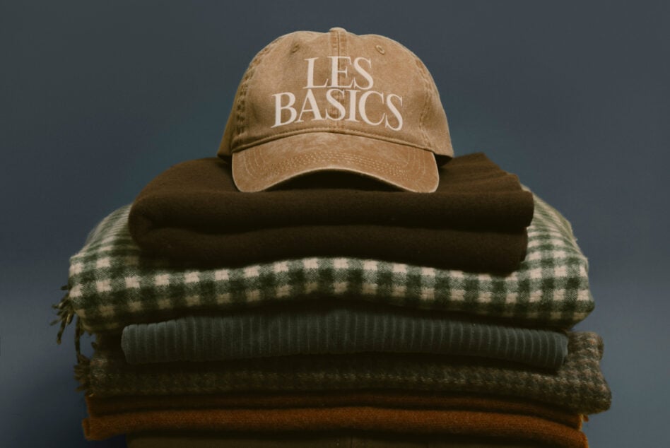 Tan vintage cap with Les Basics text on pile of knit sweaters