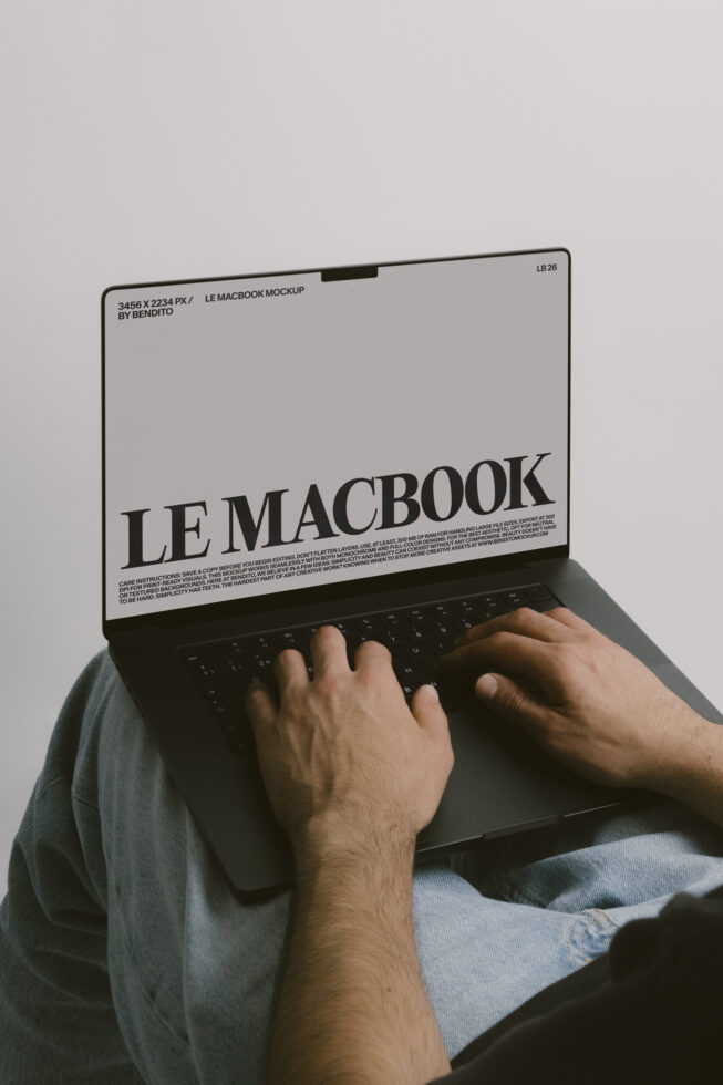 Hands typing on MacBook with neutral screen showing black serif typography