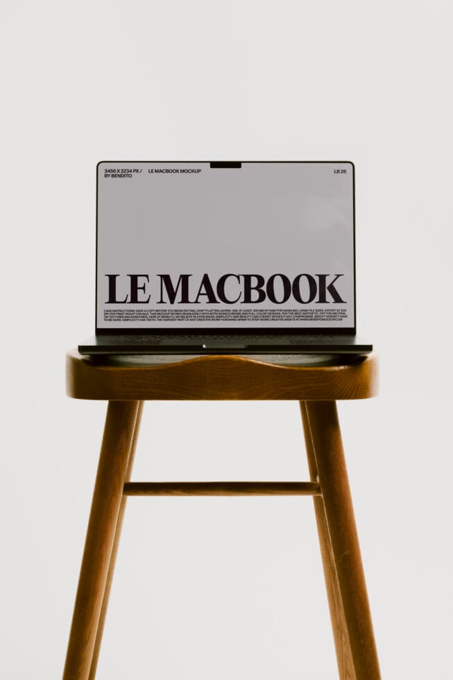 MacBook mockup on wood stool showing gray screen with black text layout