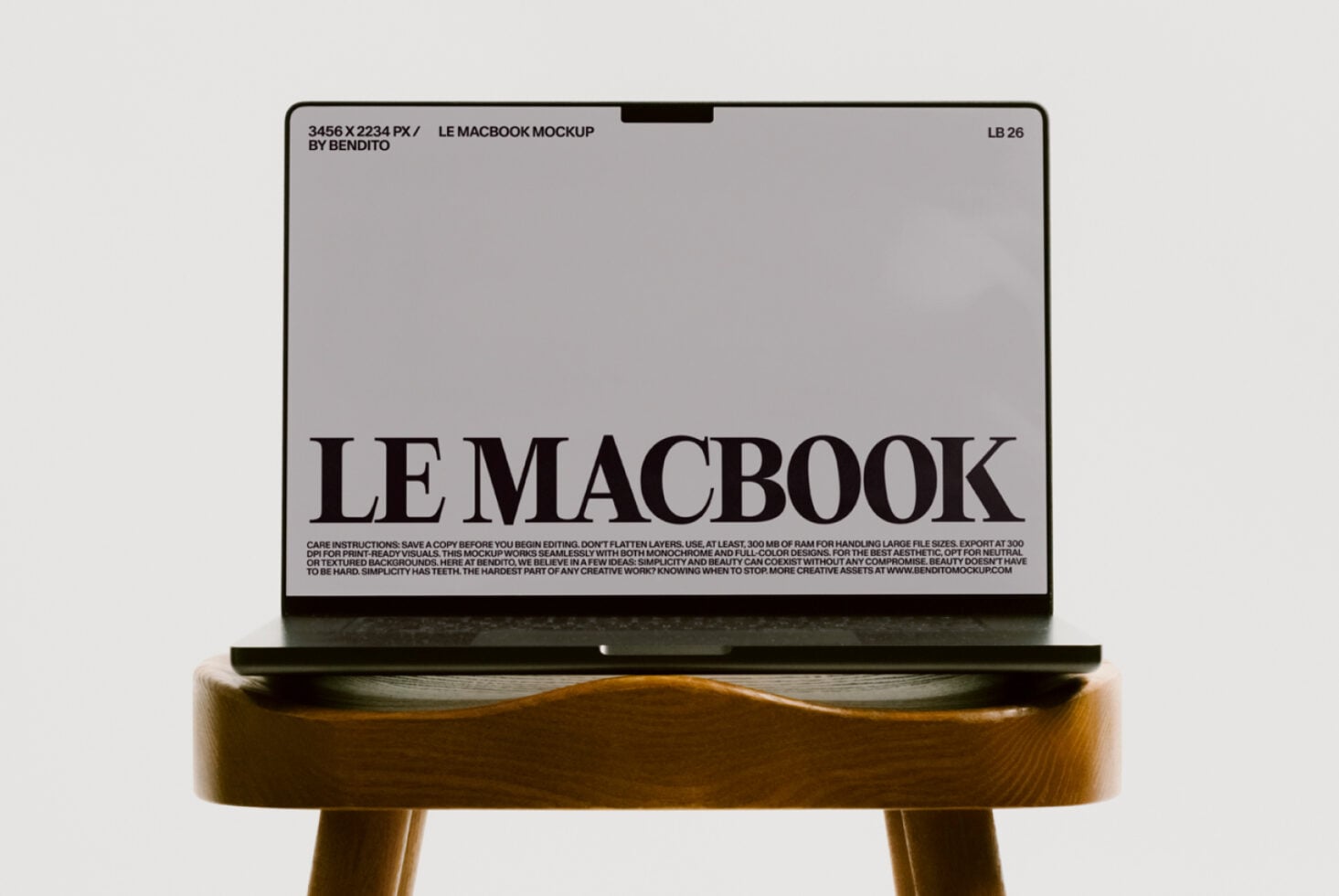 MacBook mockup on wood stool showing light gray screen with bold serif headline
