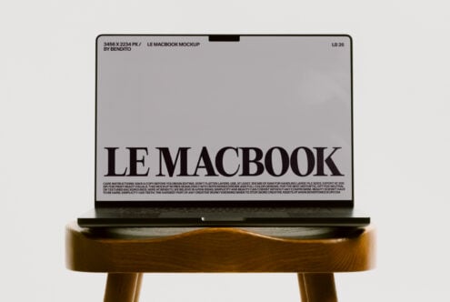 MacBook mockup on wood stool showing light gray screen with bold serif headline