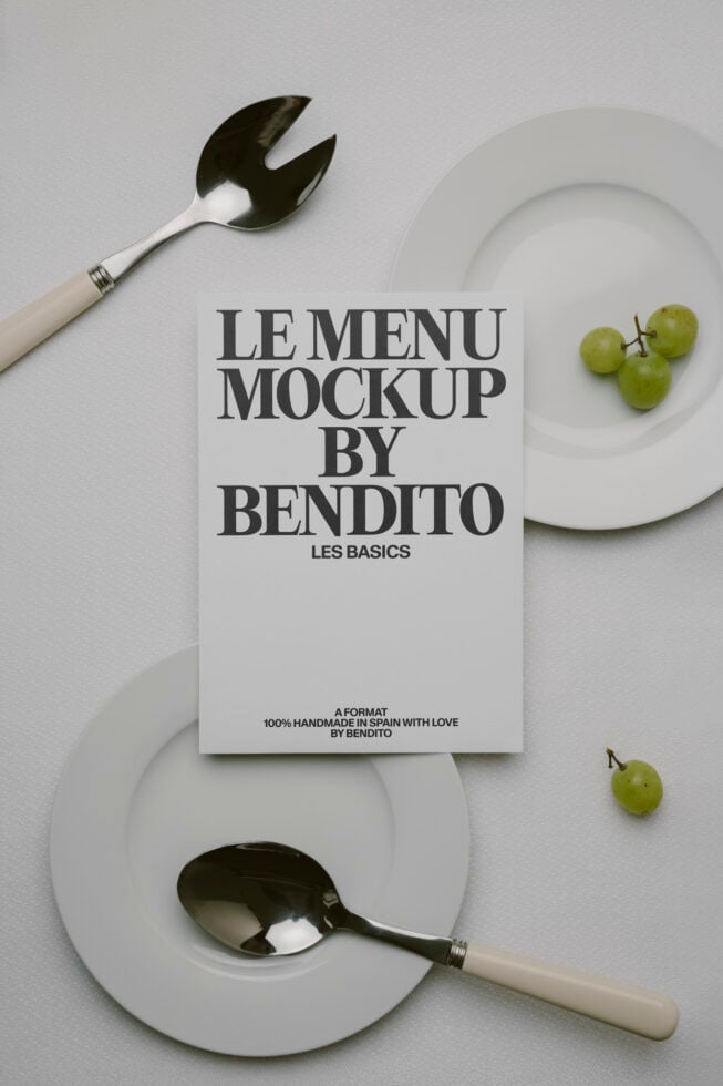 White menu card between white plates with utensils on white surface