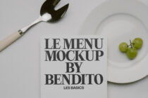 Black text menu mockup on cream card with fork, plate, grapes on white surface
