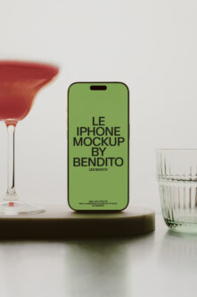 Bright green iPhone mockup centered between cocktail glass with red drink on left side