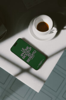 iPhone with green screen mockup on white surface next to espresso cup with shadows