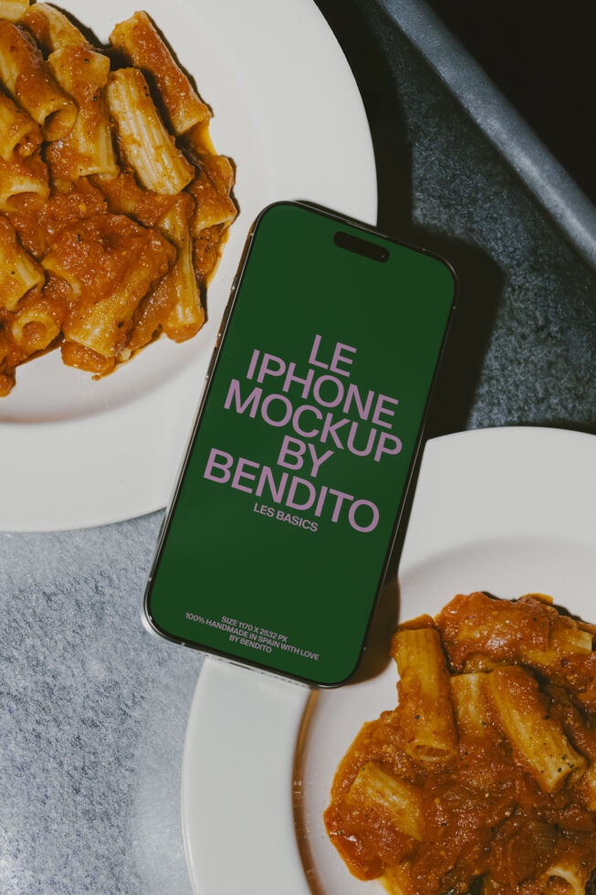 iPhone with green screen mockup surrounded by pasta dishes on marble surface