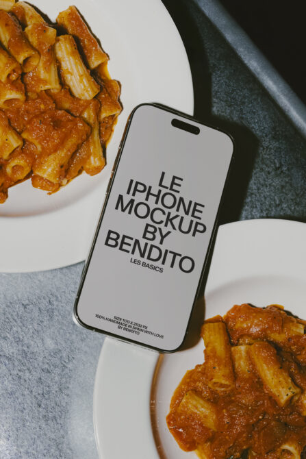 iPhone with white screen mockup surrounded by pasta dishes on marble surface