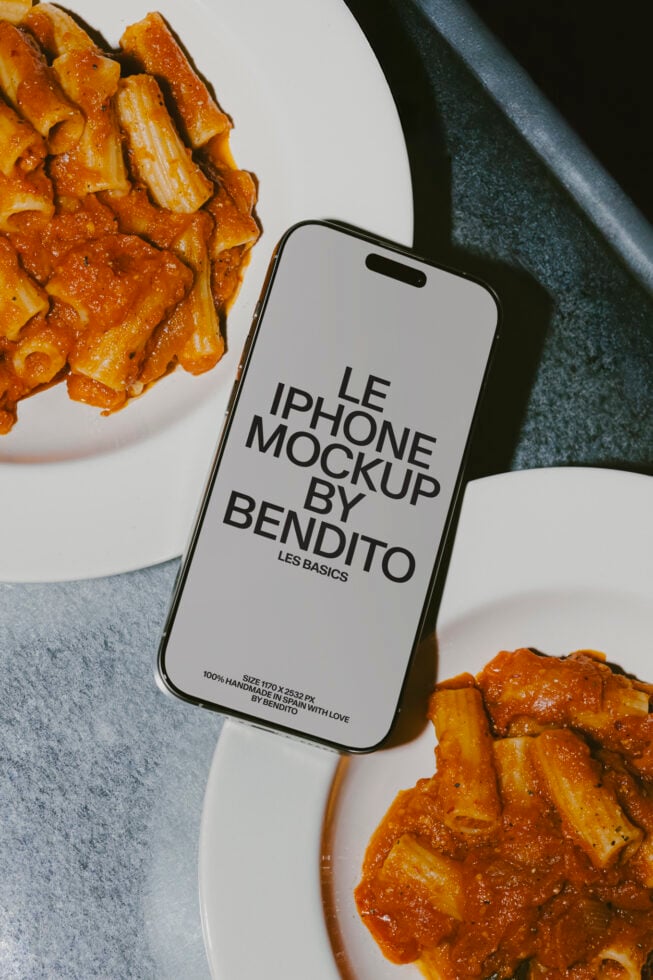 iPhone with white screen mockup surrounded by pasta dishes on marble surface