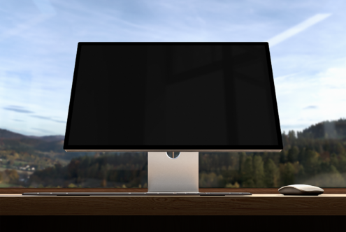 Modern computer monitor on a wooden desk with scenic forest view outside large window perfect for mockups and showcasing digital graphics assets