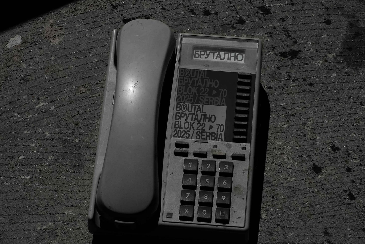 Vintage brutalist phone with keypad next to brutalist branding label on concrete
