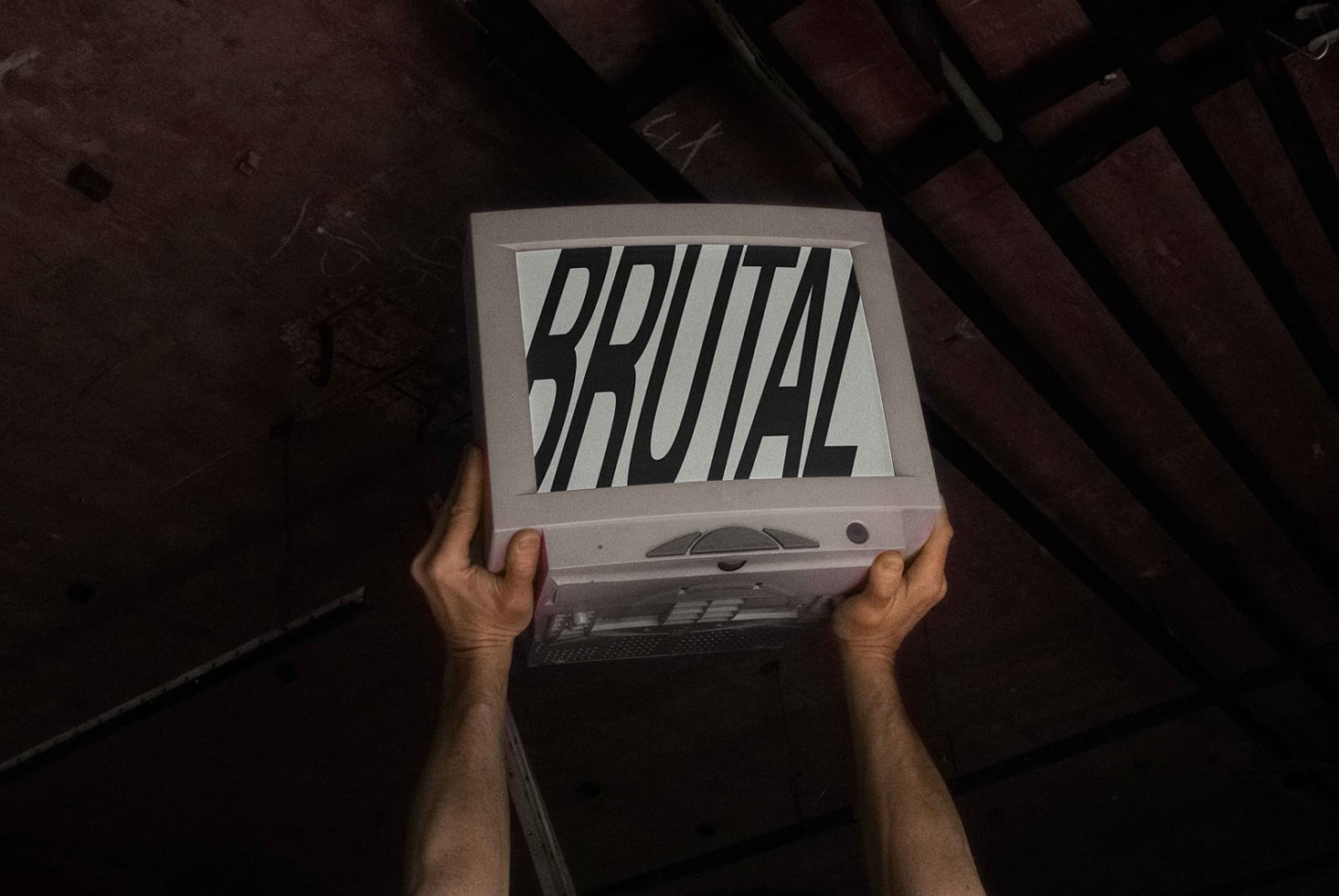 Hands holding vintage laptop screen showing Brutal typography design