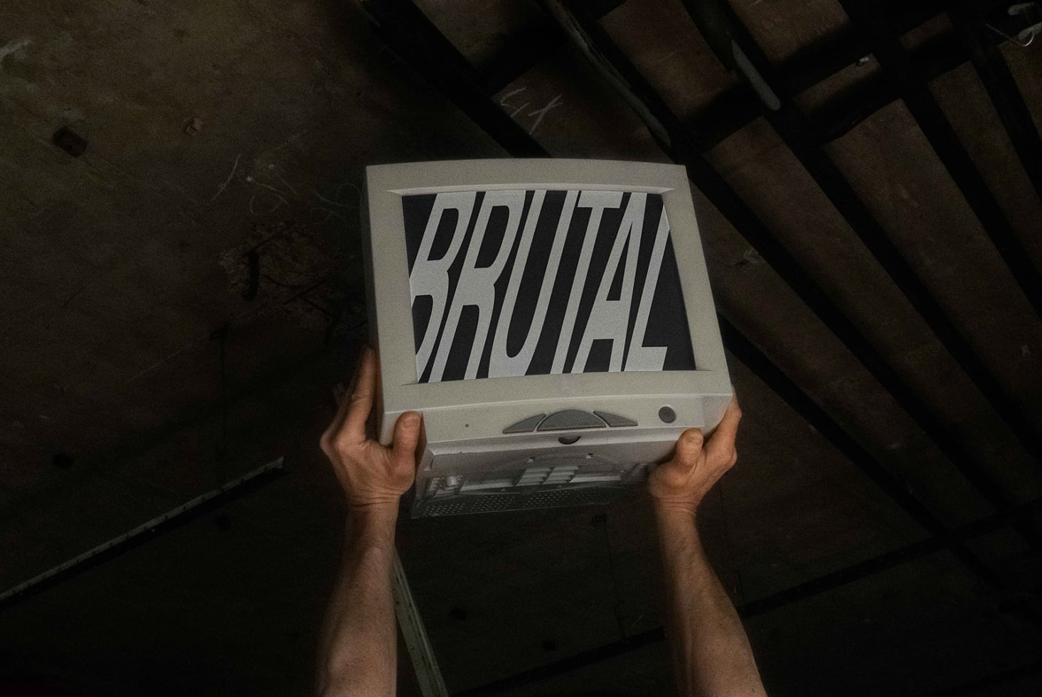 Hands holding old laptop displaying Brutal text with diagonal stripes