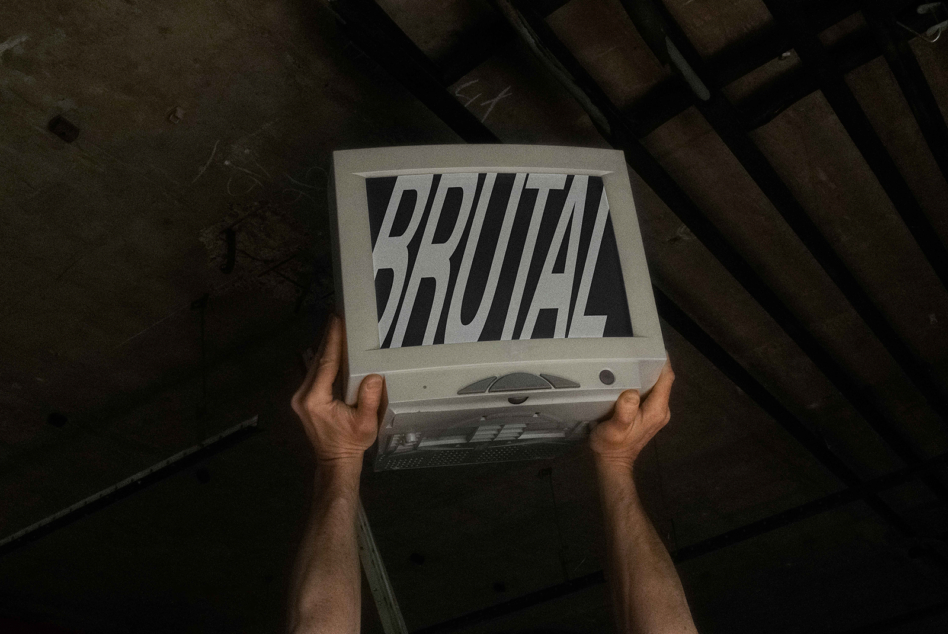 Hands holding old laptop displaying Brutal text with diagonal stripes