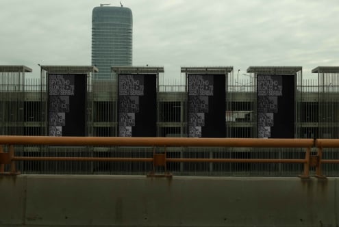 Multiple black banners on metal fence with tower behind brutal collection signage