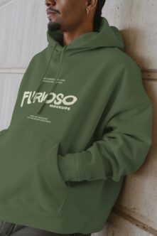 Man wearing olive green hoodie with cream Furioso logo on front, concrete wall backdrop
