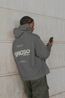 Person wearing gray hoodie holding phone showing Furioso Mockups back print