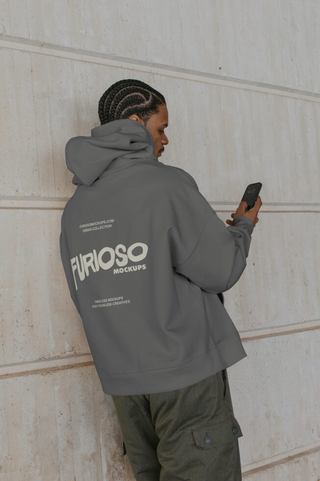 Person wearing gray hoodie holding phone showing Furioso Mockups back print