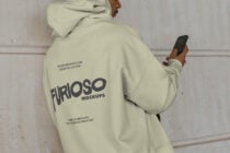 Cream hoodie side angle with person scrolling phone by wall