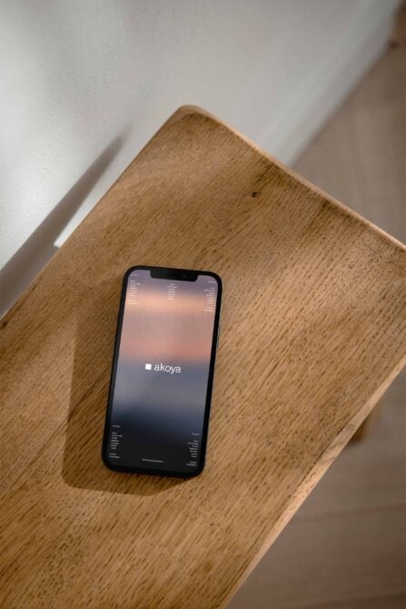 iPhone on wood table showing Akoya app with peachy gradient transitioning to dark navy background